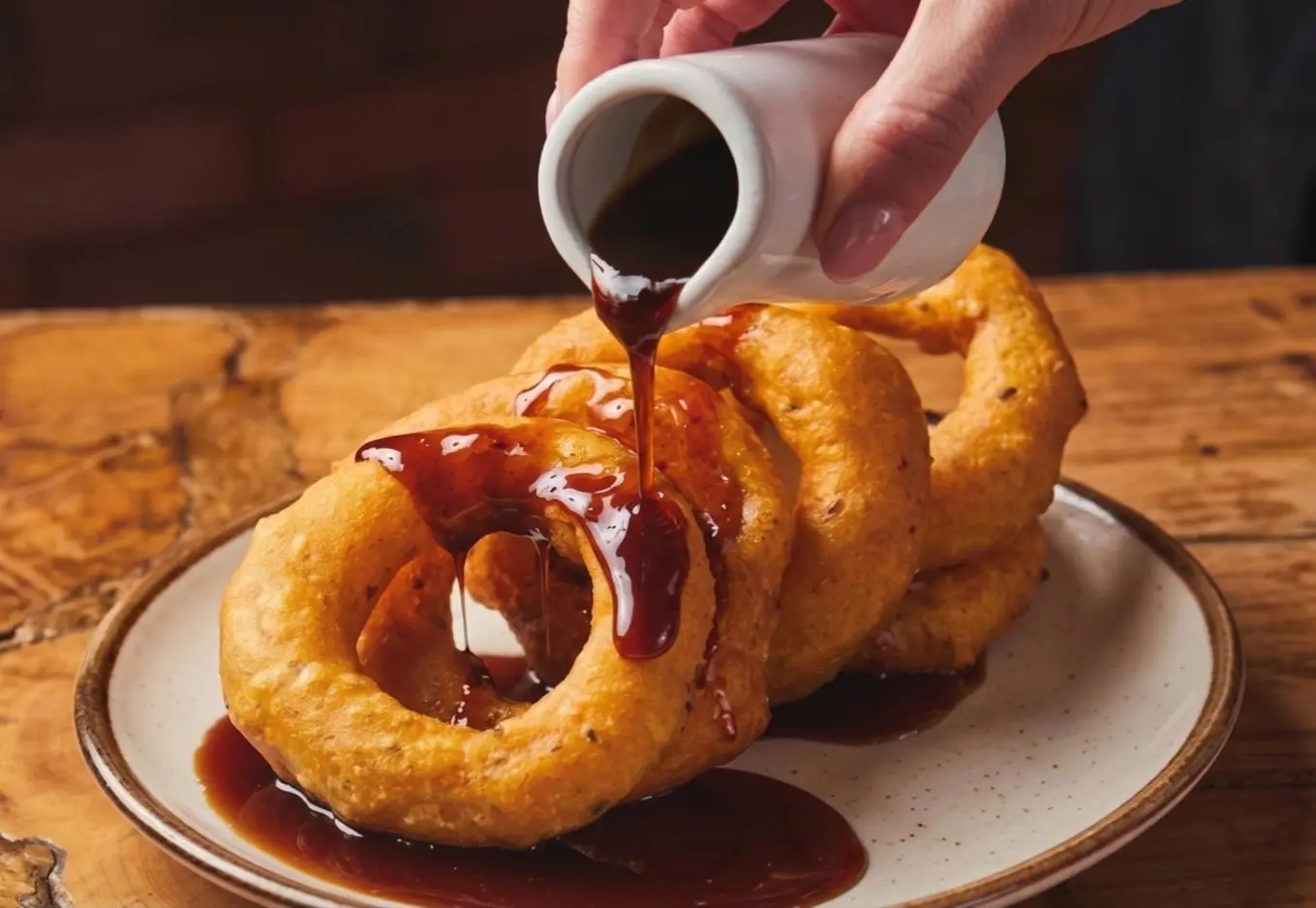 A small plate with five hot picarones — golden ring-shaped fritters — drizzled generously with dark chancaca syrup, served at a Lima street cart